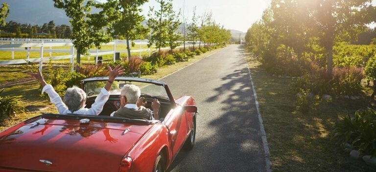 A couple in a red convertible driving down a country road.